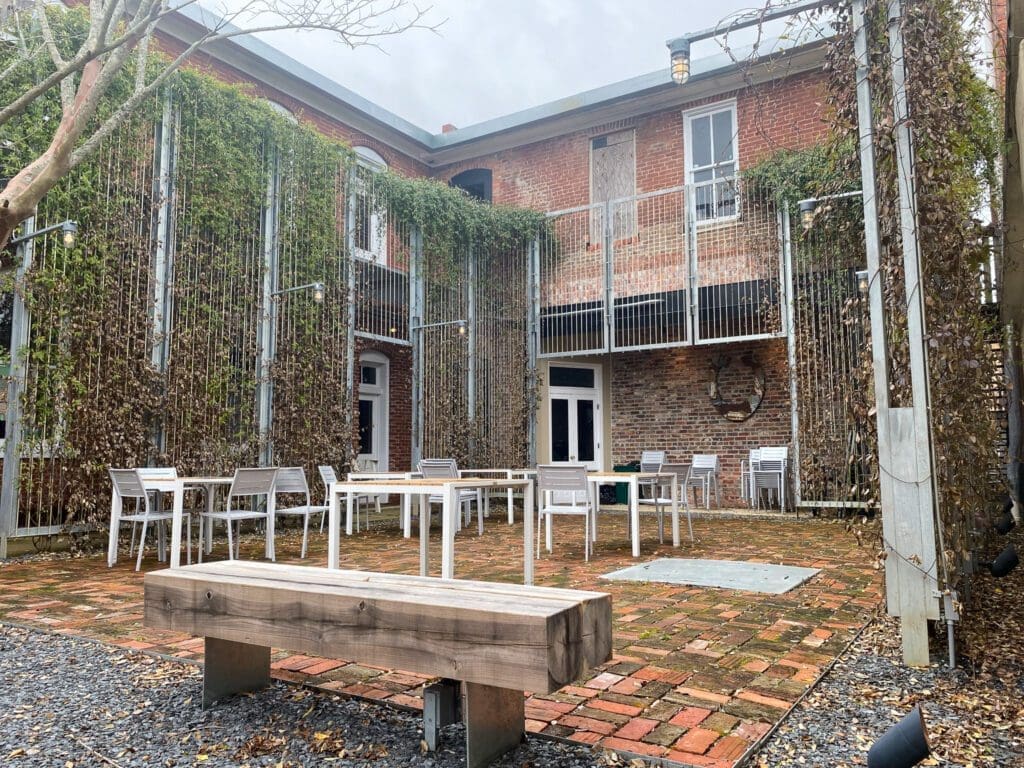 Image of the aforementioned Greensboro hanging gardens. Tall metal Trellis's surround a small brick patio with chairs and tables.