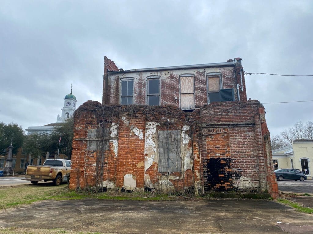 The decaying back of a brick building. It has Ivey growing over it and old windows appear to have been bricked over. 