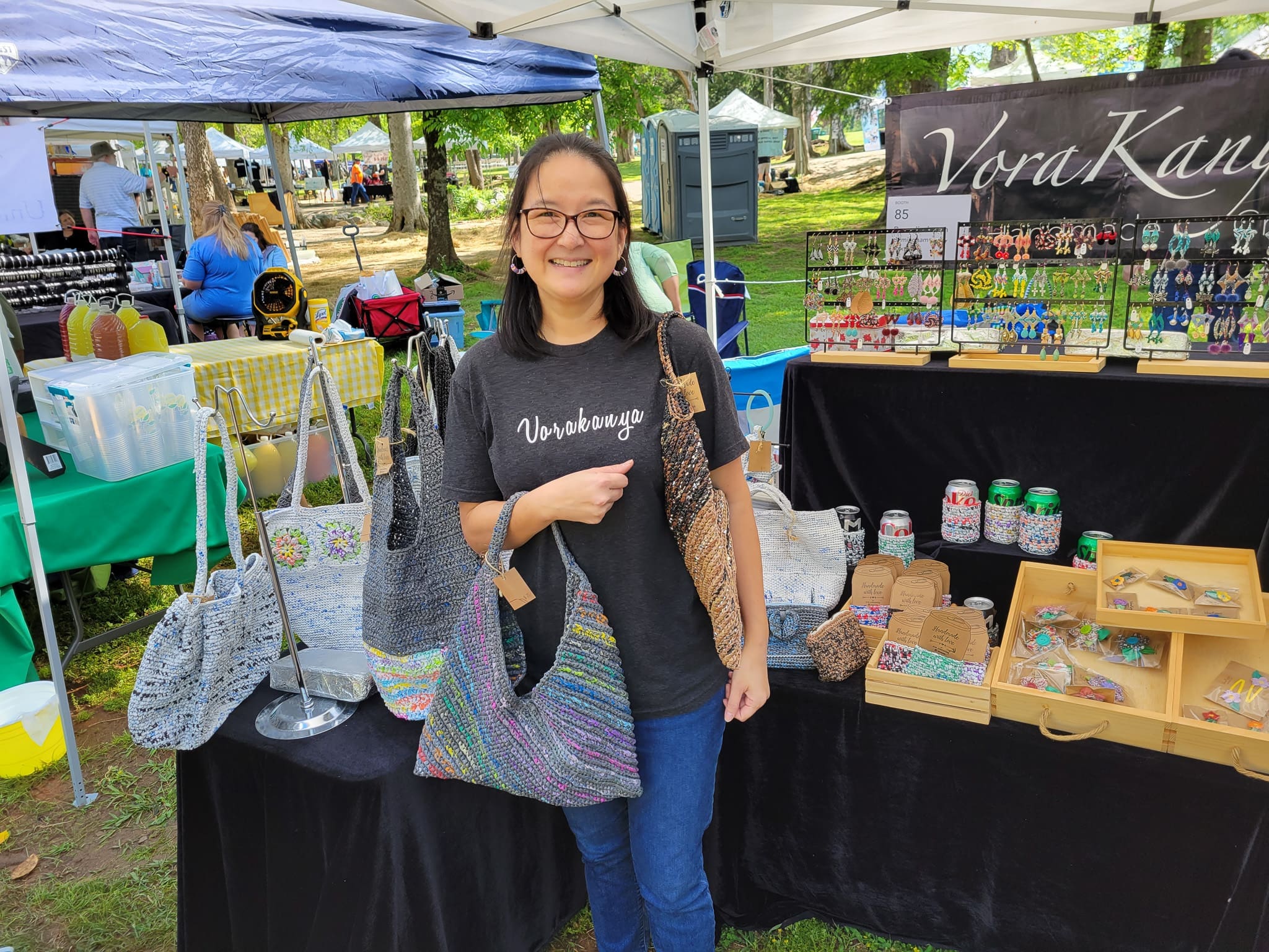 Pim Jindapon standing at her booth holding some of her bags crocheted from plastic.